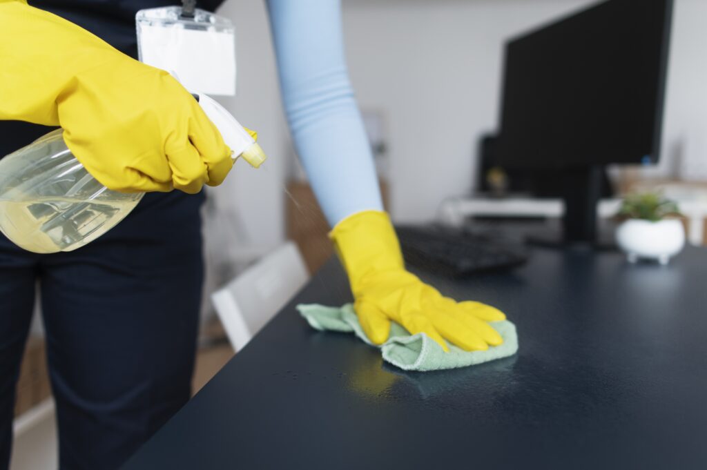 A janitorial cleaner dusting and sanitizing an office desk.