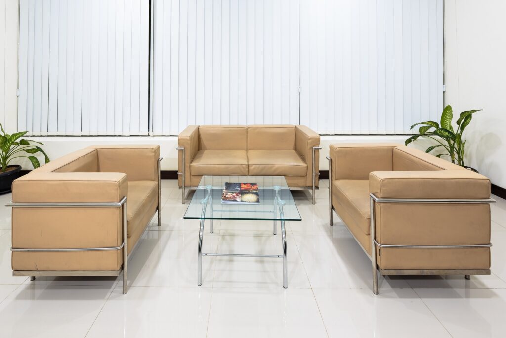 A clean, well-maintained small contemporary office lobby with three couches and a glass and chrome table.